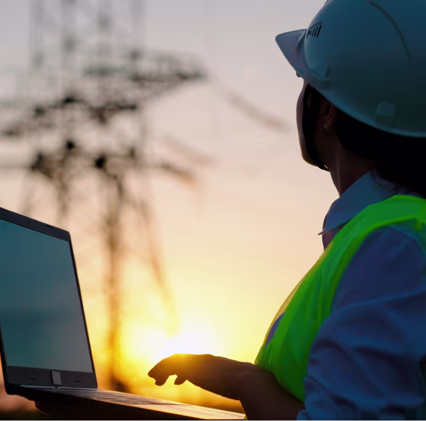 A utility inspector in a hard hat looking up at transmission infrastructure